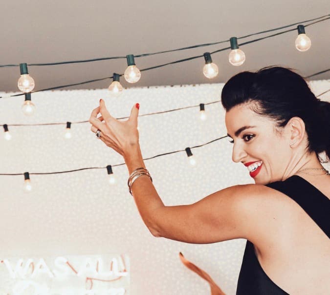 A guest laughing beneath a canopy of string lights at a Pretty Creative event